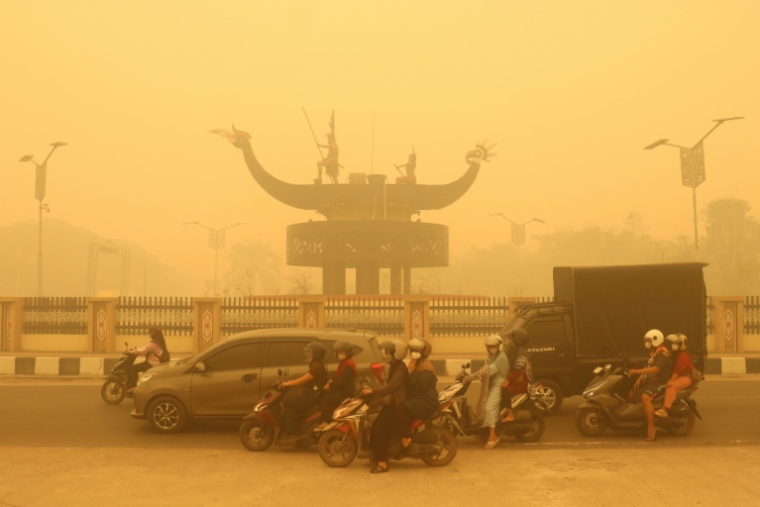 Des motocyclistes portant un masque de protection circulent dans une épaisse brume causée par des feux de forêt et de terres dans la région de Palangkaraya, dans le Kalimantan central, le 24 octobre 2026 en Indonésie ( AFP / REINA )