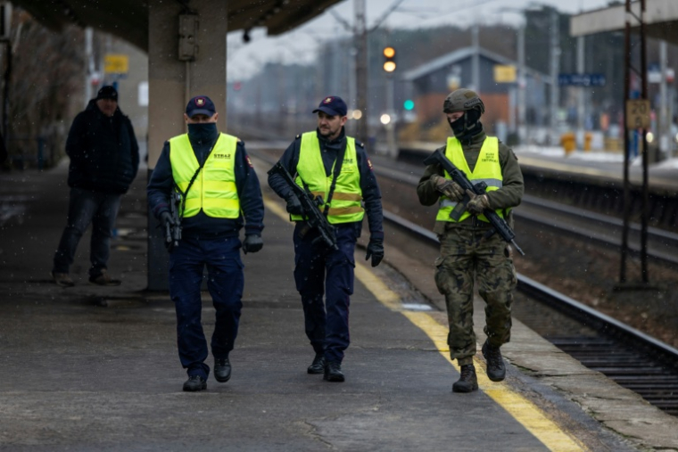Des gardes de la sécurité ferroviaire armés et un soldat des Forces de défense territoriale patrouillent sur un quai de gare dans la banlieue de Varsovie, le 27 novembre 2025 en Pologne ( AFP / Wojtek RADWANSKI )