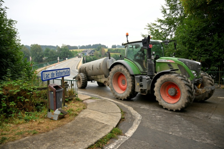 Un agriculteur conduit un tracteur équipé d'une citerne d'eau sur le barrage du lac de Robertville, à Waimes, alors qu'un incendie fait rage dans la réserve naturelle des Hautes Fagnes ,le 17 août 2026 en Belgique ( AFP / JOHN THYS )