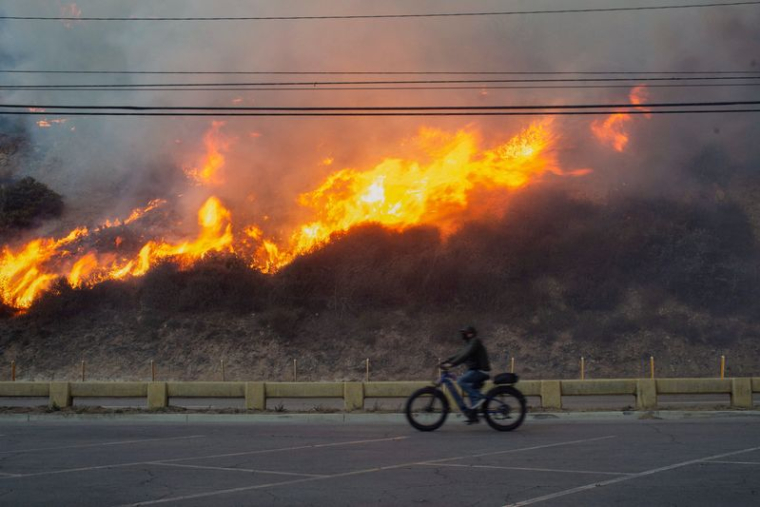 Une personne fait du vélo alors que l'incendie de Palisades brûle pendant une tempête de vent sur la côte ouest de Los Angeles