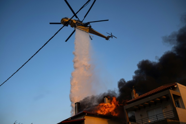 Un hélicoptère largue de l'eau sur une maison en proie aux flammes à Kryoneri, près d'Athènes, le 26 juillet 2025 ( AFP / Angelos TZORTZINIS )