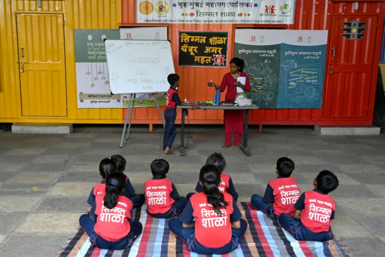 Des élèves assistent à un cours donné à "l'école du feu rouge", qui accueille des enfants défavorisés dans des conteneurs aménagés en salles de cours sous un pont autoroutier, le 18 mai 2026 à Bombay ( AFP / Punit PARANJPE )