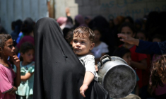 Une Palestinienne portant un enfant dans une file d'attente à un distribution de repas chauds à Nousseirat, dans le centre de la bande de Gaza, le 4 juin 2025 ( AFP / Eyad BABA )