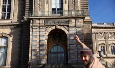 Une personne pose devant une fenêtre à l'étage qui a été brisée par des voleurs pour entrer dans le musée du Louvre