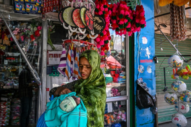 Une habitante, son enfant dans les bras, passe devant des boutiques du marché de Poonch, où le calme est revenu après le cessez-le-feu avec le Pakistan, le 11 mai 2025 en Inde ( AFP / Punit PARANJPE )