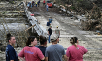 Des gens observent les forces de l'ordre et les volontaires qui recherchent des disparus près de Camp Mystic, le site où au moins 20 filles ont disparu après des inondations soudaines à Hunt, au Texas, le 5 juillet 2025 ( AFP / RONALDO SCHEMIDT )