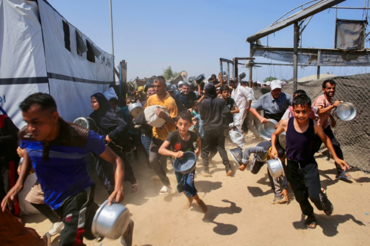 Des Palestiniens dont des enfants courent, après l'ouverture de la grille, pour aller chercher des repas auprès d'une organisation caritative locale à Khan Younès dans le sud de la bande de Gaza, le 22 juillet 2025 ( AFP / - )