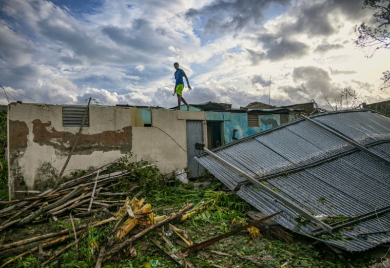 Un habitant de la ville d'El Cobre, dans la province de Santiago de Cuba, marche sur le toit de sa maison endommagée après le passage de l'ouragan Melissa, le 29 octobre 2025. ( AFP / YAMIL LAGE )