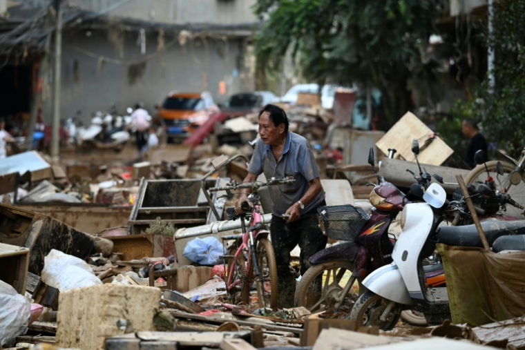 Un habitant pousse son vélo au milieu des débris dans une zone inondée après la rupture d'un réservoir près de Gantang, dans la région du Guangxi, le 9 juillet 2026 dans le sud-ouest de la Chine ( AFP / GREG BAKER )