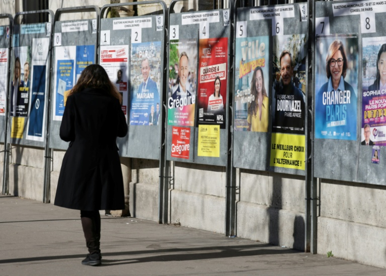 Une femme passe devant un panneau électoral avec les candidats à la mairie de Paris, le 9 mars 2026, à Paris ( AFP / Ludovic MARIN )