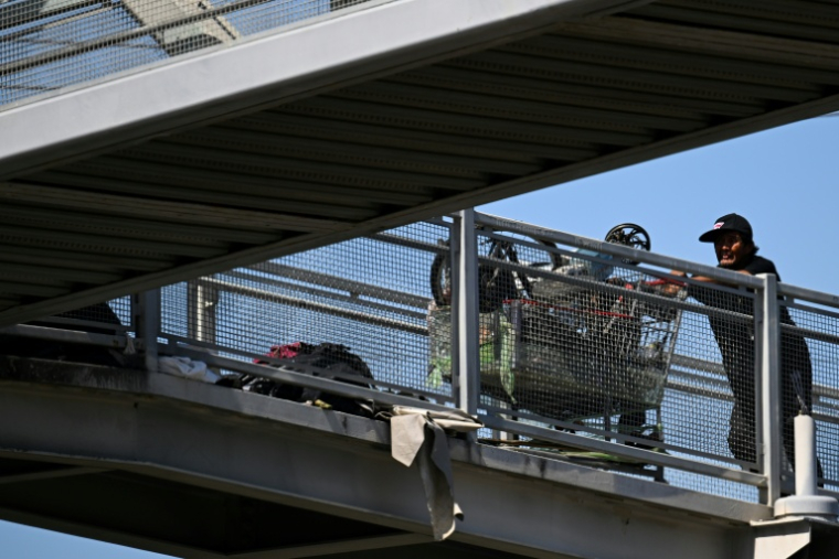 Un sans-abri pousse un chariot rempli d'affaires, sur un pont près d'un campement de SDF, à Los Angeles, le 1er juin 2026 ( AFP / Patrick T. Fallon )