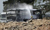 Un pompier israélien arrose une carcasse de bus après le tir d'un missile iranien à Herzliya, près de Tel-Aviv, le 17 juin 2025 ( AFP / Jack GUEZ )