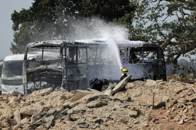 Un pompier israélien arrose une carcasse de bus après le tir d'un missile iranien à Herzliya, près de Tel-Aviv, le 17 juin 2025 ( AFP / Jack GUEZ )