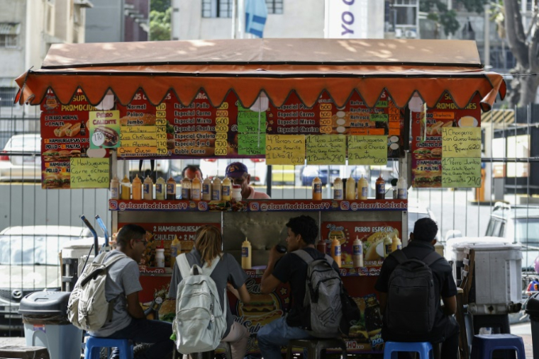Des clients mangent à une échoppe de rue où les prix sont affichés en bolivars (monnaie officielle vénézuélienne) à Caracas, Venezuela, le 2 juin 2025 ( AFP / Pedro MATTEY )