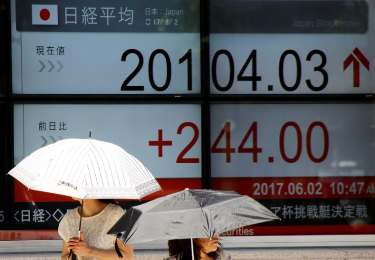 Des femmes munies d'ombrelles passent devant un panneau d'affichage électronique indiquant l'indice Nikkei japonais, à l'extérieur d'une société de courtage à Tokyo