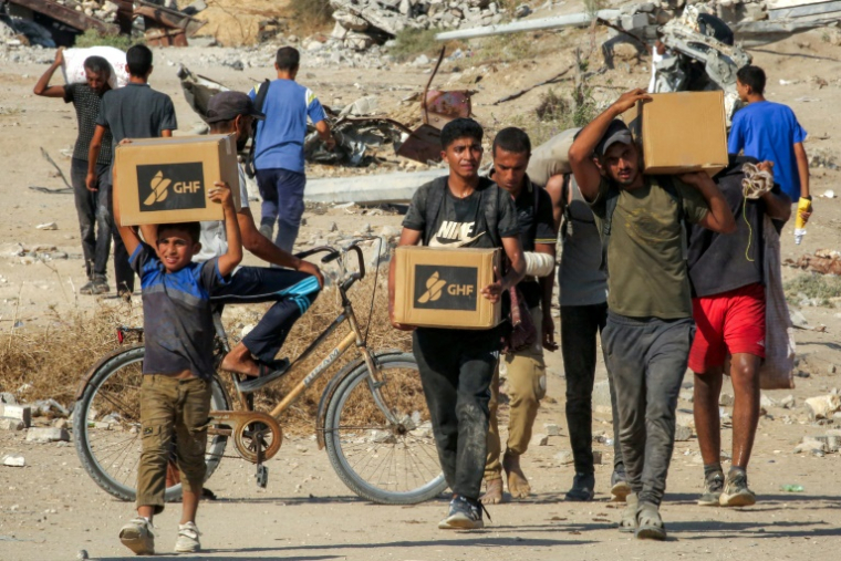 Des Palestiniens portent des cartons d'aide humanitaire reçus dans un centre de distribution géré par la Fondation humanitaire de Gaza (GHF), alors qu'ils traversent le "corridor de Netzarim", dans le centre de la bande de Gaza, le 22 août 2025 ( AFP / Eyad BABA )