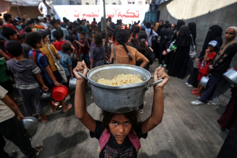 Une fillette porte sur sa tête une marmite de riz distribué par une cuisine caritative dans le camp de réfugiés de Nousseirat, dans le centre de la bande de Gazale, 14 septembre 2025 ( AFP / Eyad BABA )