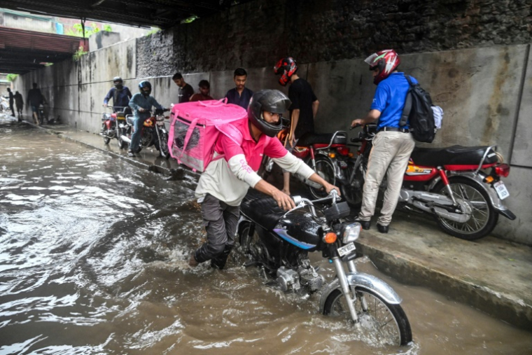 Abdullah Abbas (c), livreur de repas, pousse sa moto dans une rue inondée après de fortes pluies à Lahore, le 30 août 2025 au Pakistan ( AFP / Aamir QURESHI )