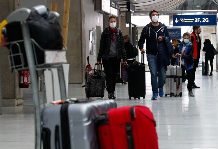 Des personnes portant des masques de protection arrivent à l'aéroport Charles de Gaulle près de Paris