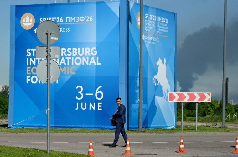 Un homme passe devant des affiches du Forum économique international de Saint-Pétersbourg alors que de  la fumée s'élève en arrière-plan après des frappes de drones ukrainiens, le 3 juin 2026 ( AFP / STRINGER )