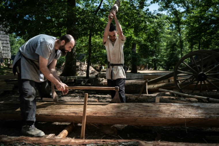 Des charpentiers fendent un tronc d'arbre sur le chantier de construction du château de Guédelon à Treigny, le 23 juin 2025 dans l'Yonne ( AFP / ARNAUD FINISTRE )