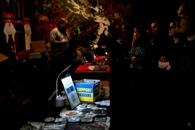 Des indications pour faire des dons à l'Ukraine sont disposées sur une table avec des produits dérivés du groupe de metal ukrainien "1914" avant un concert à Varsovie, le 25 mars 2026 ( AFP / Sergei GAPON )