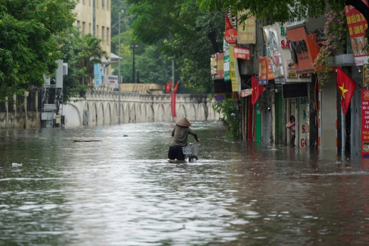 Une habitante pousse son vélo dans une rue inondée à Hanoï, après le passage du typhon Kajiki, le 26 août 2025 au Vietnam ( AFP / Minh Tri )