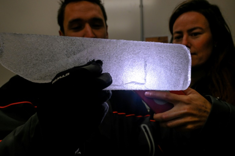 Des scientifiques examinent à la lumière d'un téléphone portable une carotte glaciaire antarctique dans un laboratoire à Bruxelles, le 15 juillet 2025 en Belgique ( AFP / Nicolas TUCAT )