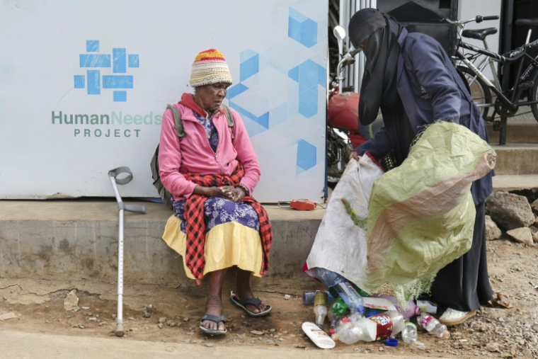 Molly Aluoch (c) remet un sac de déchets plastiques usagés à un responsable de l'ONG Human Needs Project (HNP) dans le bidonville de Kibera, à Nairobi, le 11 août 2025 au Kenya ( AFP / Tony KARUMBA )