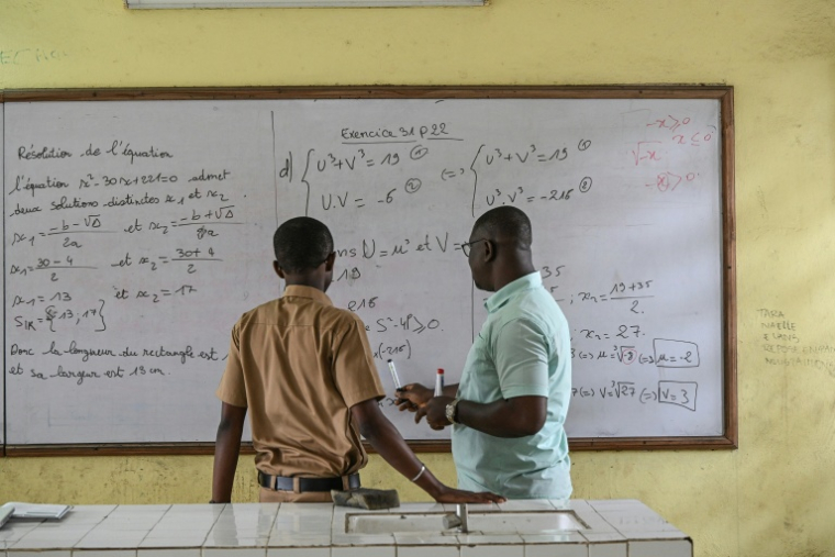 Un professeur de mathématiques (à droite) explique un exercice à un élève de terminale scientifique dans un lycée du quartier de Cocody, à Abidjan (Côte d'Ivoire), le 22 septembre 2026 ( AFP / Sia KAMBOU )