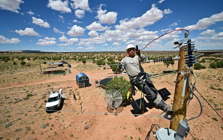Cole Garcia, ouvrier de l'entreprise Mohave Electric, travaille sur un poteau électrique pour raccorder les maisons d'Amérindiens Navajo à Tonalea, en Arizona, le 8 juillet 2025 ( AFP / Frederic J. BROWN )