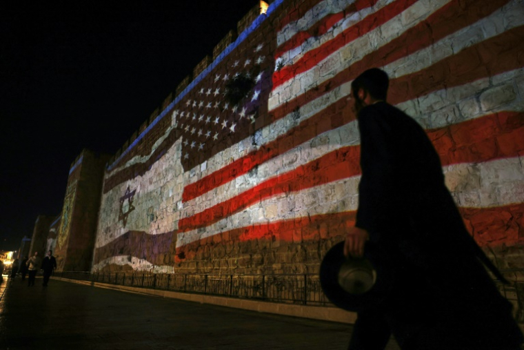 Des gens passent devant une projection représentant des drapeaux israélien et américain sur les murs de la vieille ville de Jérusalem, le 22 juin 2025 ( AFP / AHMAD GHARABLI )