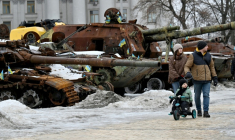 Un couple et un enfant à vélo se promènent dans l'exposition en plein air d'équipements militaires russes détruits à Kiev, le 15 février 2026 ( AFP / Sergei SUPINSKY )