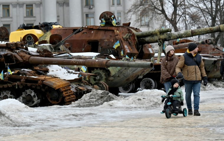 Un couple et un enfant à vélo se promènent dans l'exposition en plein air d'équipements militaires russes détruits à Kiev, le 15 février 2026 ( AFP / Sergei SUPINSKY )