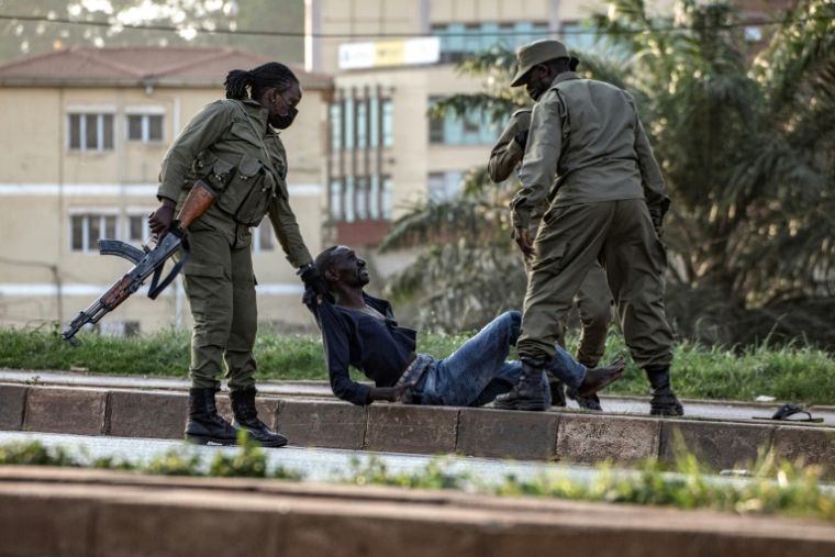 Des policiers interpellent un électeur au sol près d'un bureau de vote à Kampala le 15 janvier 2026, pendant les élections  ( AFP / BADRU KATUMBA )