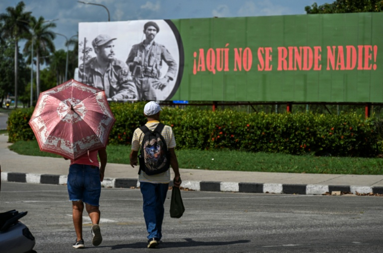 Des Cubains devant une affiche à l'effigie du défunt dirigeant cubain Fidel Castro (1926-2016) et du commandant Juan Almeida Bosque (1927-2009) sur laquelle est écrit "Ici, personne ne se rend", le 19 juin 2026 à La Havane  ( AFP / YAMIL LAGE )
