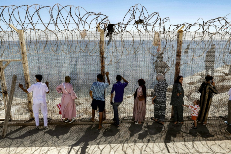 Des personnes attendent derrière une clôture surmontée de barbelés le retour de proches ayant tenté de franchir la frontière pour entrer dans l’enclave espagnole de Ceuta, le 2 août 2026 à Fnideq ( AFP / Abdel Majid BZIOUAT )
