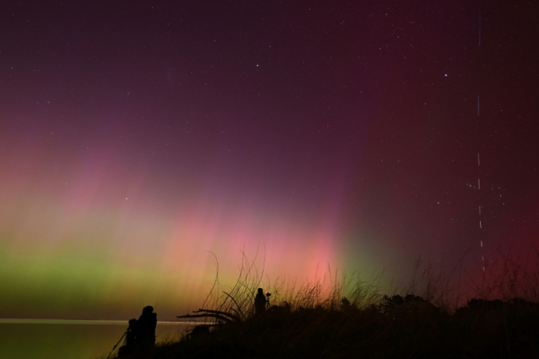 Une traînée lumineuse de satellites Starlink (d) pendant une aurore australe, ou aurore du Sud, au-dessus des eaux du lac Ellesmere, près de Christchurch, le 11 mai 2024 en Nouvelle-Zélande ( AFP / Sanka Vidanagama )
