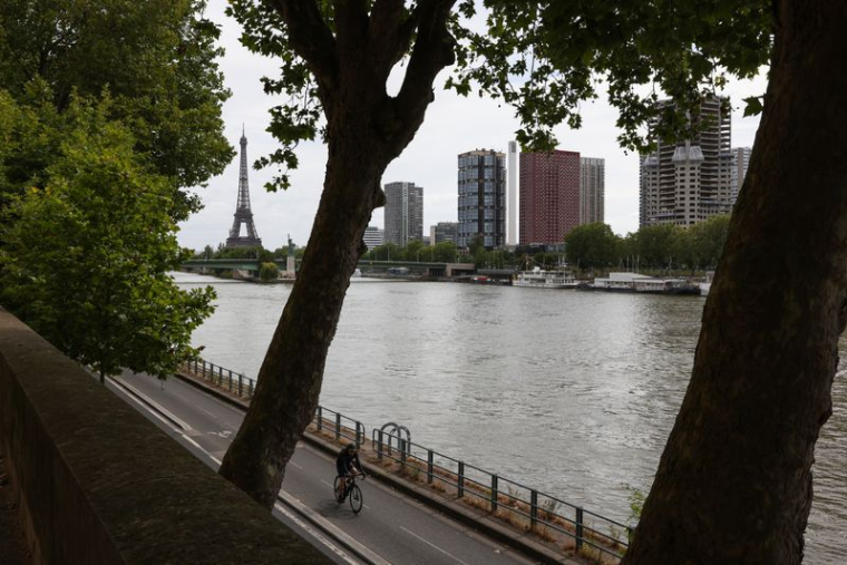 Un homme roule à vélo sur les rives de la Seine avec la Tour Eiffel en arrière-plan