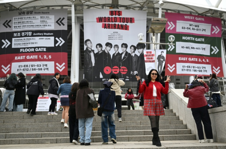 Des fans posent pour des photos devant une grande banderole à l'effigie du boys band de K-pop BTS, sur les marches menant au stade où le groupe se produira, à Goyang, le 9 avril 2026 ( AFP / Jung Yeon-je )