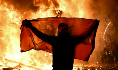 Un manifestant tient un drapeau albanais devant un kiosque en flammes pendant une manifestation antigouvernementale à Tirana, le 15 octobre 2026  ( AFP / Armend NIMANI )