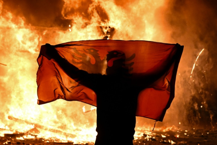 Un manifestant tient un drapeau albanais devant un kiosque en flammes pendant une manifestation antigouvernementale à Tirana, le 15 octobre 2026  ( AFP / Armend NIMANI )
