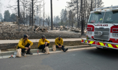 Trois membres du service d'incendie de Spokane en pause sur le bord du trottoir devant des maisons d'habitation incendiées, dans le quartier de Balboa à Spokane (Washington), le 2 août 2026 ( AFP / Erick Doxey )