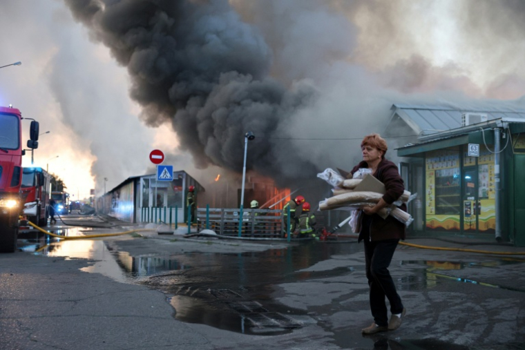 Une femme près d'un épais panache de fumée s'élevant depuis un marché aux livres après une attaque aérienne russe, le 16 août 2026 à Kiev  ( AFP / STRINGER )
