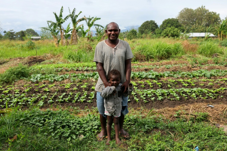 Dennis Phillip et son fils Kayddy dans leur potager où des dizaines de bombes américaines non explosées de la Seconde Guerre mondiale ont été retrouvées, le 11 septembre 2025 à Honiara, aux Iles Salomon ( AFP / Ben STRANG )