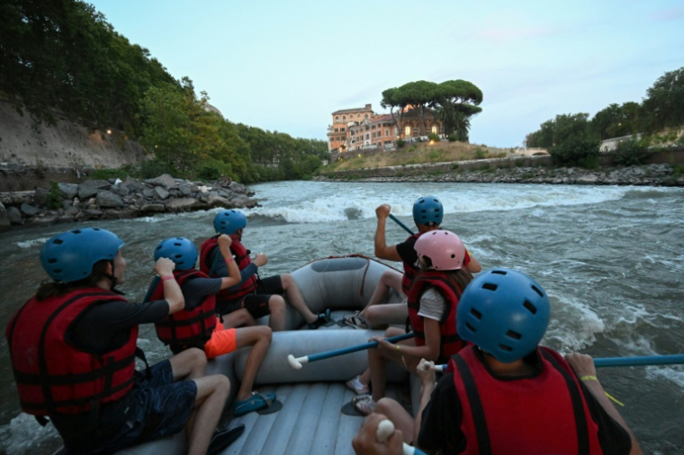 Des personnes naviguent en canot pneumatique sur le Tibre, passant devant l'île Tibérine, sur un tronçon du fleuve situé entièrement dans la zone urbaine du centre de Rome, le 14 août 2026 ( AFP / Andreas SOLARO )