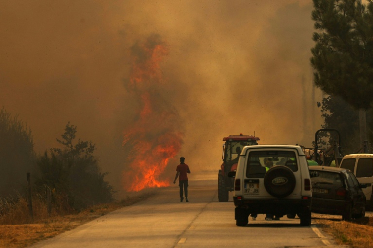 Un homme se dirige vers les flammes sur une route couverte de fumée dans le village d'Antas au Portugal, le 15 août 2025 ( AFP / PATRICIA DE MELO MOREIRA )