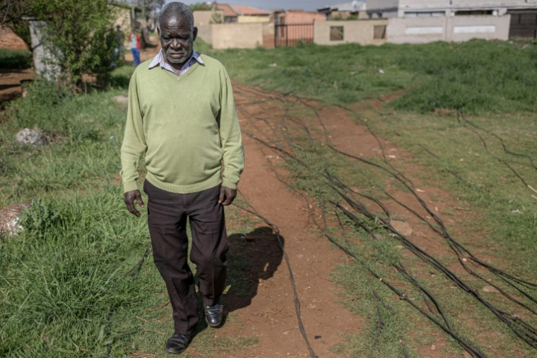 Un habitant du township de Katlehong, près de Johannesburg, marche à côté des câbles qui raccordent illégalement son quartier au réseau électrique, le 5 octobre 2026 ( AFP / EMMANUEL CROSET )