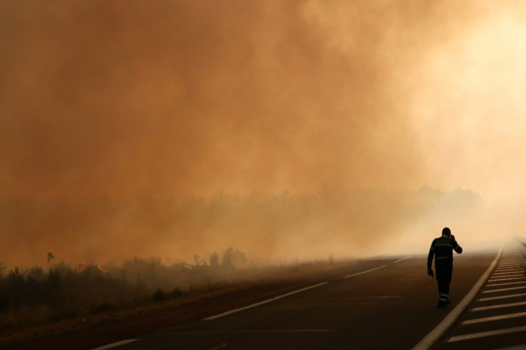 Un pompier marche sur une route à la lisière d'une zone en feu à Ares, le 26 juillet 2026, alors qu'un incendie de forêt ravage la forêt au nord du bassin d'Arcachon (Gironde) depuis le 22 juillet ( AFP / ROMAIN PERROCHEAU )