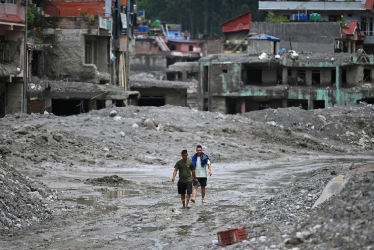 Des habitants traversent, le 30 août 2026, une rue ensevelie sous des tonnes de boue du centre de Trishuli, au Népal, victime d'une crue dévastatrice ( AFP / Arun SANKAR )